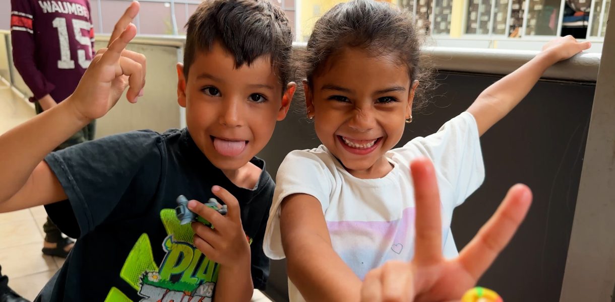 Dos niños migrantes sonríen alegremente mientras juegan en el patio de la Casa Migrante Arcángel Rafael, un refugio que brinda apoyo y esperanza a familias en tránsito.